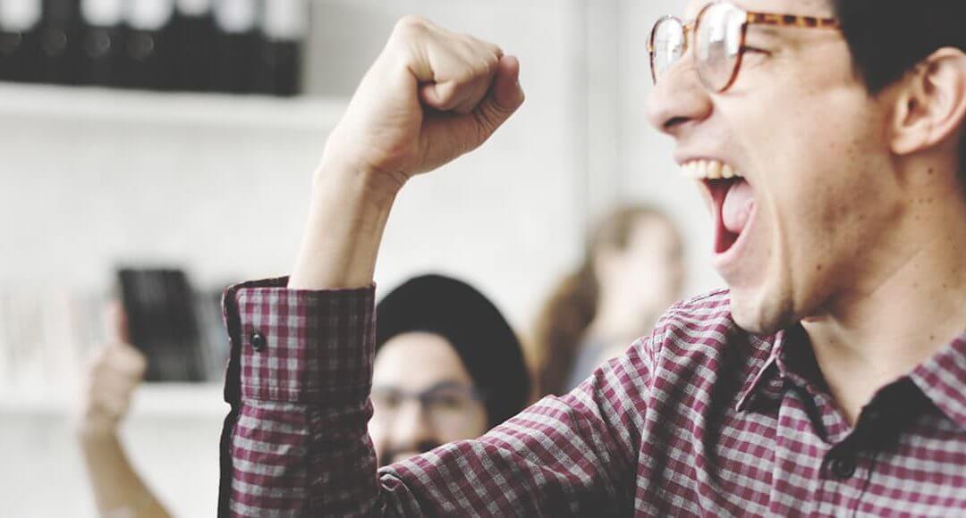 Startup Life Hacks image - bespectacled man in shirt fist pumps in an office