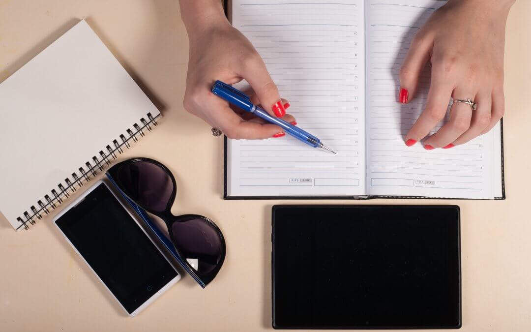 Start-Up Efficiency: 6 of the best free apps for a productive day. Photo - Woman writing in diary with a tablet, sunglasses and another notebook