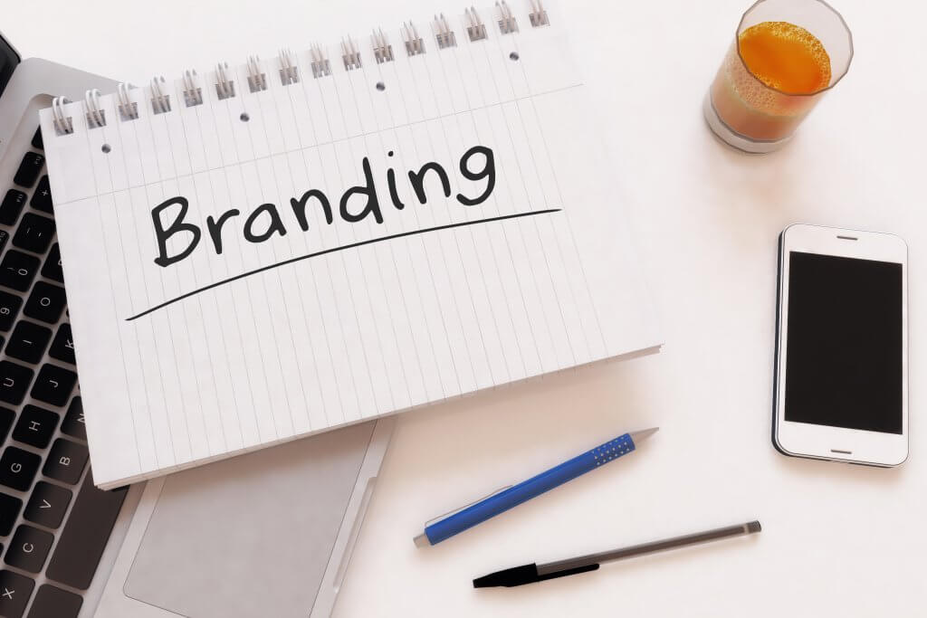 Naming Your Brand - Image - Notepad with branding written on it, plus a glass of juice, a phone and pens on a desk